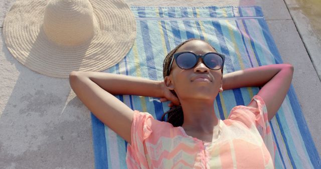 African American woman wearing sunglasses relaxing on a blanket outdoors on a sunny day. Can be used for themes related to summer activities, leisure, vacation getaways, relaxing outdoors, beach relaxation, and enjoying warm weather.