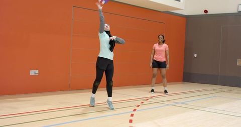 Indian and african american women playing badminton in indoor gym executing jump smash