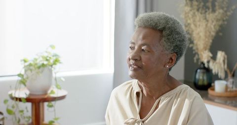 Senior african american woman sitting by window in minimalist living room, serene portrait