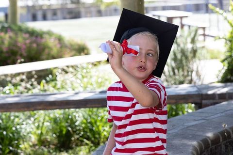Preschool boy celebrating milestone wearing graduation cap and holding diploma outdoors