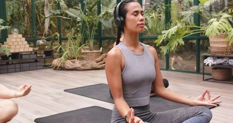 Woman Practicing Mindfulness Meditation with Headphones in Glass-Encased Garden