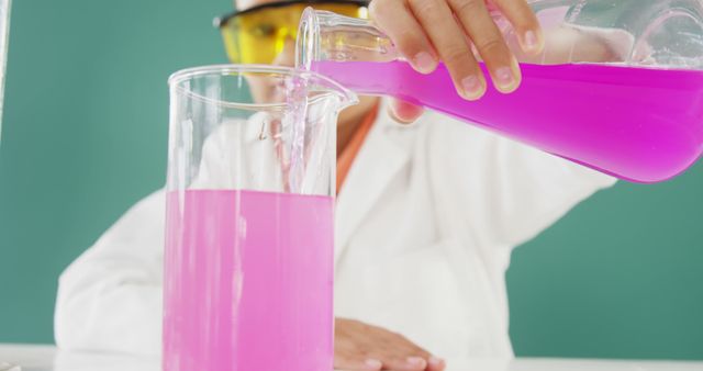 Scientist in white coat and safety glasses pouring pink liquid into beaker. Image captures critical moment in laboratory experiment. Perfect for educational materials, scientific blogs, and chemistry-related content.