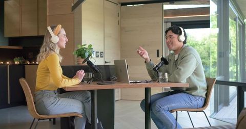 Co-hosts recording podcast conversation in modern home studio with headphones and microphones