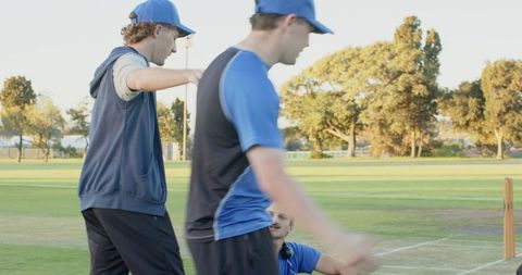 Male cricket team discussing tactics with coach during practice on green grass pitch