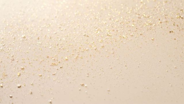 Shimmering gold leaf flakes on smooth beige surface luxury background with sparkle