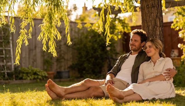 Couple relaxing under willow tree in sunlit backyard embracing quiet romantic moment
