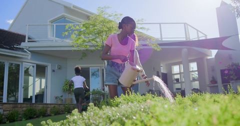 Teen girl watering front yard garden at modern house on sunny afternoon