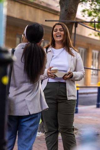 African american friends laughing and chatting on urban sidewalk holding takeaway coffee
