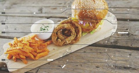 Serving sesame-seed cheeseburger with crispy onion rings and sweet potato fries on rustic plank