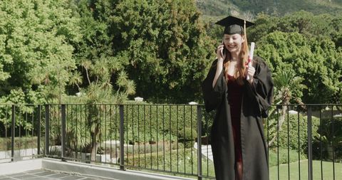 Graduate calling while holding diploma on sunlit terrace overlooking lush garden