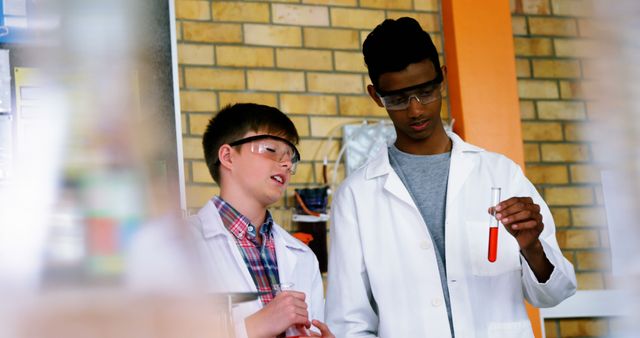 Two teenage boys, wearing lab coats and safety goggles, conducting a chemistry experiment with test tubes in a school laboratory. One of the boys is holding a red liquid filled test tube while the other one is observing intently. Perfect for educational materials, science-related articles, or school project demonstrations.