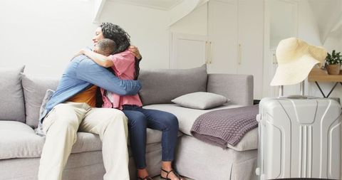 Couple hugging at home with packed suitcase indicating departure