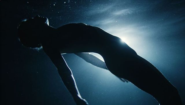Backlit silhouette swimmer floating underwater with dramatic rim light and particles