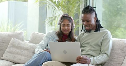 Couple sharing laptop on sofa in modern bright living room with plants