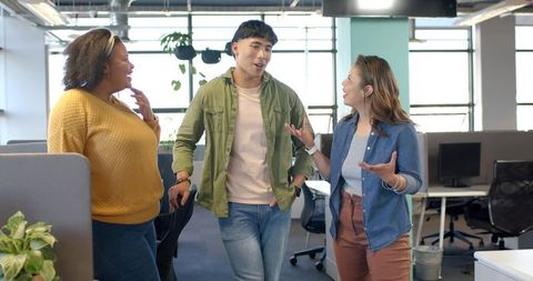 Diverse coworkers walking and talking in bright modern open office, casual teamwork