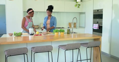 African american mother and teen daughter preparing healthy salad at modern kitchen island