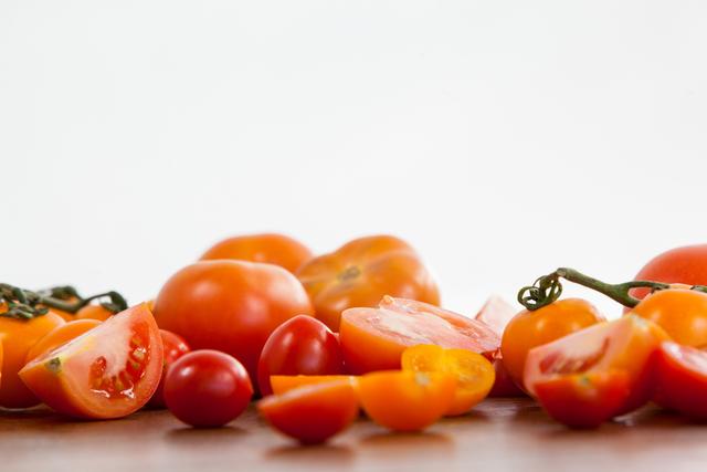 Various types of tomatoes, including red and yellow, whole and sliced, are displayed on a wooden table. This image can be used for promoting healthy eating, organic food, cooking recipes, nutrition blogs, and grocery store advertisements.