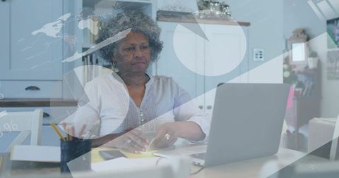 Senior woman working on laptop arranging sticky notes for budgeting and planning at kitchen table