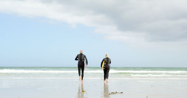 Older couple in wetsuits going surfing at the beach on a cloudy day - Download Free Stock Images Pikwizard.com