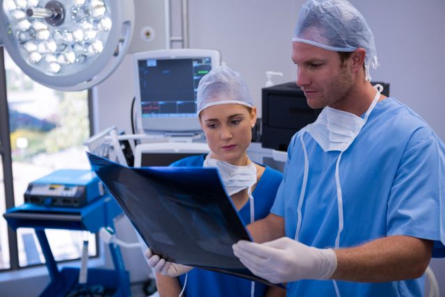 Medical professionals in surgical attire are examining an x-ray in an operating room. This image can be used for healthcare-related content, medical articles, hospital brochures, or educational materials about medical procedures and teamwork in healthcare settings.