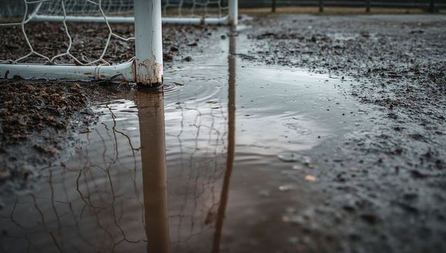Muddy soccer goalpost reflecting in rain puddle on wet pitch with net detail