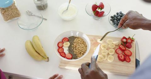 Couple preparing colorful granola bowl with sliced banana strawberries blueberries