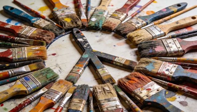 Worn Paintbrushes Forming Peace Sign on Paint-Splattered Artist Worktable, Colorful Ring