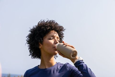 African american woman drinking from reusable bottle while wearing smartwatch outdoors
