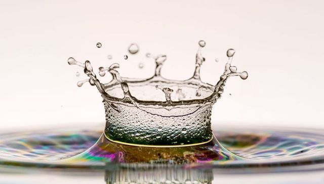 Droplet crown forming with iridescent rainbow ripples macro water splash detail