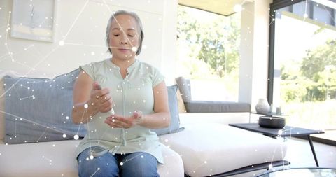 Senior asian woman dispensing hand sanitizer on sofa practicing home hygiene and wellness