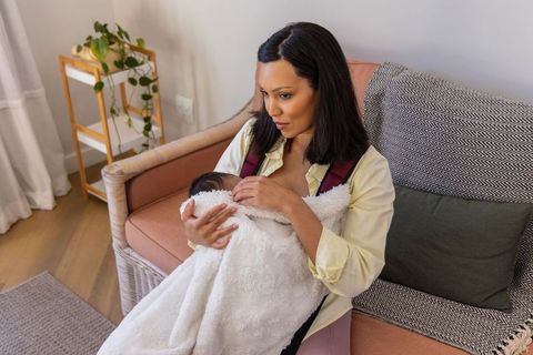 Young mother cradling swaddled newborn on cozy sofa, soothing for bonding and nurturing