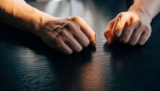 Clenching fists resting on dark wood table conveying tension and determination