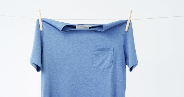 A blue t-shirt hangs on a clothesline against a plain background, with copy space. Its simple presentation suggests a focus on minimalism or the concept of laundry and clothing care.