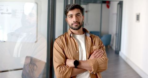 Confident entrepreneur standing arm-crossed in modern office hallway