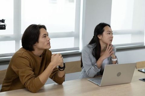 Asian coworkers listening attentively during boardroom meeting with laptop and camera