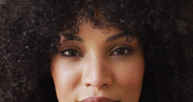 This close-up photo of a woman with curly hair showcases her natural beauty and confidence. Ideal for advertisements, beauty editorials, skincare products, haircare campaigns, diverse representation in marketing, and lifestyle blogs. The focus on her eyes and lips highlights her facial features, making it suitable for makeup promotions and emotional storytelling.