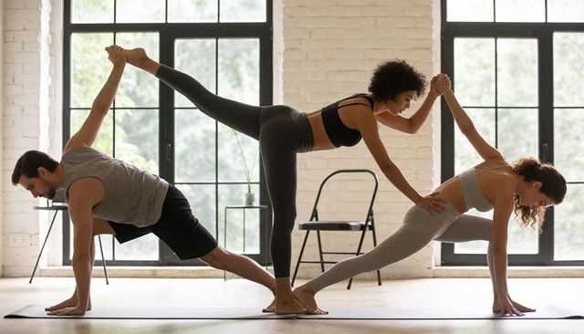 Balancing trio performing partner yoga in sunlit studio building strength and flexibility