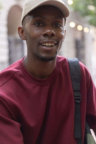 African american man smiling in beige cap maroon sweatshirt urban portrait with bokeh lights