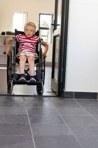 Young boy maneuvering wheelchair through home doorway showing mobility and independence