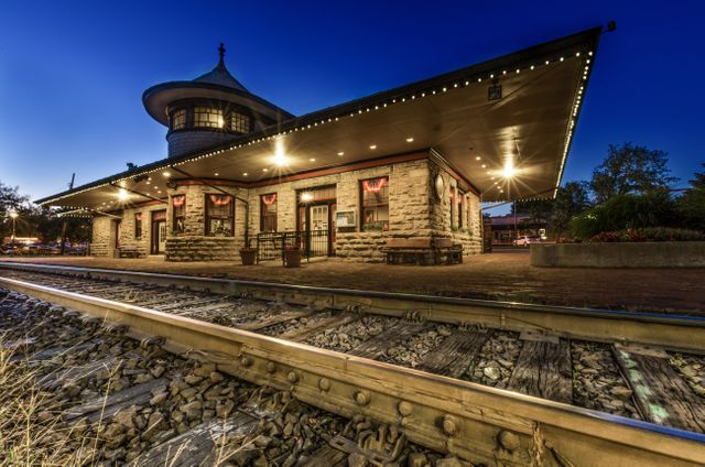 Historic train station captured during evening with charming lighting. Ideal for marketing materials for tourism, transportation schedules, and architecture appreciation days. Great for backgrounds in travel literature, heritage site promotions, and train enthusiast publications.
