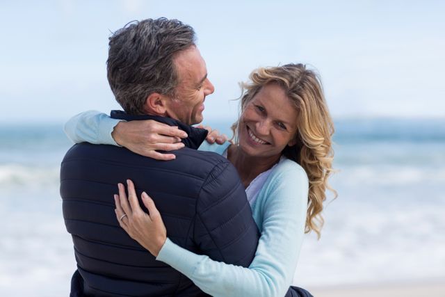 Mature couple embracing joyfully on a beach, showcasing their love and happiness. Ideal for themes of romance, senior lifestyles, vacation, and relationships. Perfect for advertising family holidays, retirement, and joyful living.