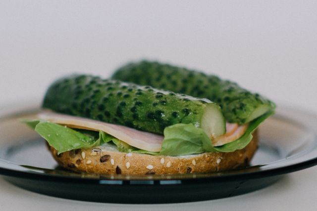 Close-up of a seeded bagel filled with fresh cucumbers, ham, and lettuce. Ideal for use in food blogs, healthy eating promotions, sandwich recipes, and healthy snack idea features.