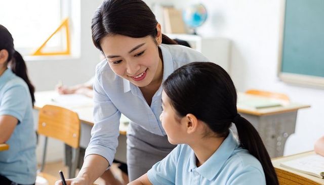 Teacher Guiding Student at Desk Smiling while Explaining Lesson in Modern Classroom