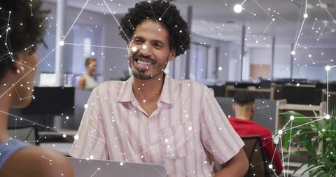 Smiling man collaborating in modern open-plan office with laptop and digital network overlay