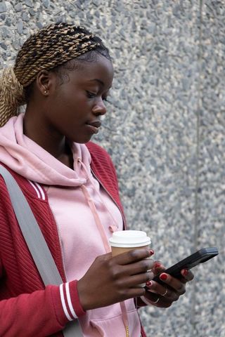 African american teen checking smartphone while holding coffee in urban streetwear