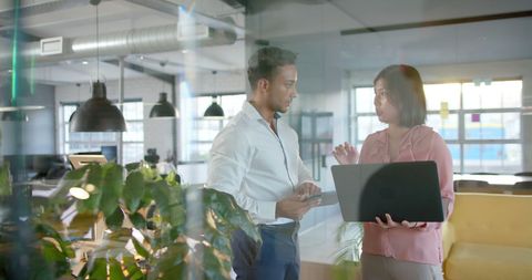 Colleagues collaborating with laptop in modern office space