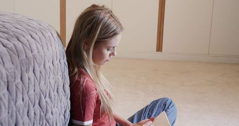 Teenager Relaxing on Floor Using Tablet Leaning Against Quilted Sofa in Minimalist Home
