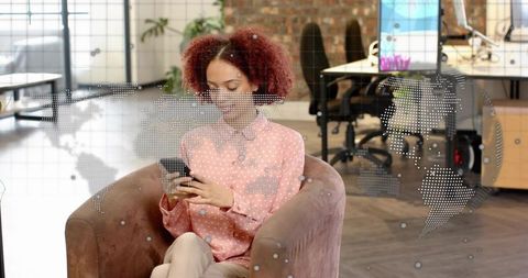 Young professional using smartphone in modern office lounge with dotted global map overlay