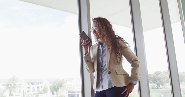 Businesswoman Using Voice Command Feature on Mobile Phone Near Large Office Windows - Download Free Stock Images Pikwizard.com