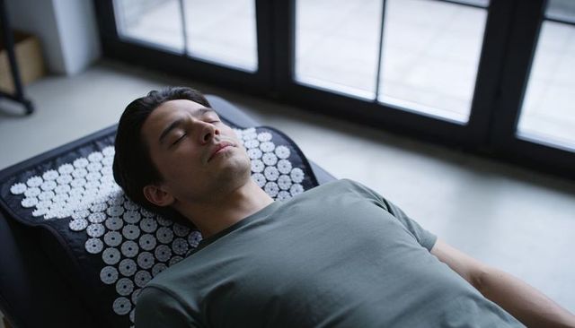 Man resting on acupressure mat for relaxation and pain relief near bright window at home